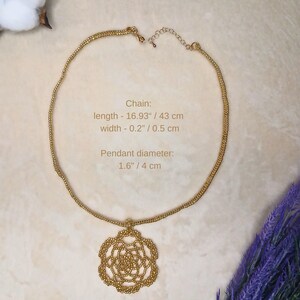 May include: A gold-colored necklace with a floral pendant. The chain is 16.93 inches (43 cm) long and 0.2 inches (0.5 cm) wide. The pendant has a diameter of 1.6 inches (4 cm). The necklace is displayed on a neutral background.