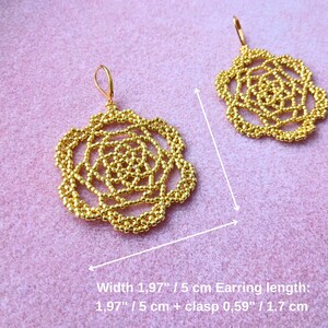 May include: A pair of gold-colored beaded earrings. Each earring has a floral design with a width of 1.97 inches (5 cm) and a length of 1.97 inches (5 cm) plus a 0.59 inch (1.7 cm) clasp. The earrings are displayed on a pink surface.