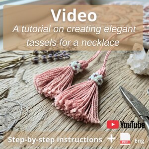 May include: Two dusty pink thread tassels attached to matching cords, each featuring a decorative bead cap made of small white and purple seed beads. The text Video A tutorial on creating elegant tassels for a necklace is visible.