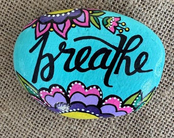 Arte rupestre pintado a mano, piedra relajante con la frase "respira" y un colorido diseño floral.
