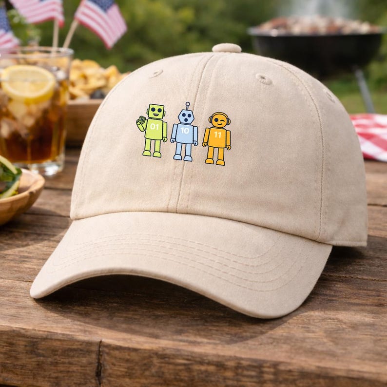 May include: A beige baseball cap with three cartoon robots in yellow, blue, and yellow. The robots have the numbers 01, 10, and 11 on their chests. The cap has a curved peak and a fabric strap.