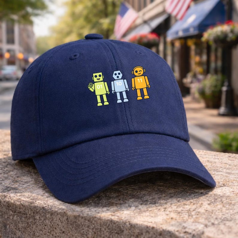 May include: A navy blue baseball cap with three robot designs in yellow, light blue, and orange. Each robot has a different design and the numbers 01, 10, and 11. The cap is made of a soft material and has a curved peak.