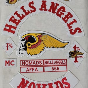May include: A collection of embroidered patches featuring the words "HELLS ANGELS" in red, arched over a central skull with wings. Additional patches include "NOMADS", "MC", "666", and "AFFA". The patches are white with red and gold accents.