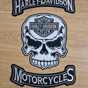 Pode incluir: Três patches da Harley-Davidson. O patch central é uma caveira com o logotipo da Harley-Davidson. Acima e abaixo estão patches curvos com as palavras "HARLEY-DAVIDSON" e "MOTORCYCLES" em letras brancas.