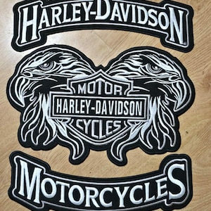 Puede incluir: Tres parches bordados de Harley-Davidson. El parche superior dice "HARLEY-DAVIDSON" en letras blancas sobre un fondo negro. El parche central presenta dos cabezas de águila y las palabras "MOTOR HARLEY-DAVIDSON CYCLES". El parche inferior dice "MOTORCYCLES".
