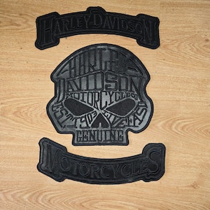 Può includere: Tre toppe nere Harley-Davidson. La toppa più grande ha la forma di un teschio con le parole "HARLEY-DAVIDSON MOTORCYCLES GENUINE" all'interno. Due toppe più piccole riportano le scritte "HARLEY-DAVIDSON" e "MOTORCYCLES".