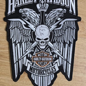 Op de afbeelding: Een zwart-wit Harley-Davidson-patch met een schedel, vleugels en bliksemschichten. De patch bevat de woorden "HARLEY-DAVIDSON" en "MOTORCYCLES". Het ontwerp is geborduurd met gedetailleerde stiksels.