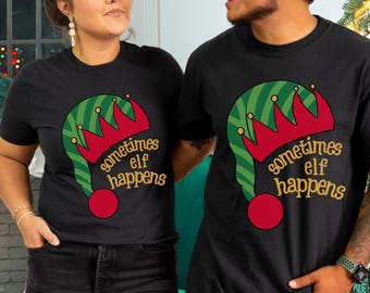 May include: Black t-shirts with a Christmas elf hat design. The hat is green and red with the text "sometimes elf happens" in gold. The shirts are short-sleeved and worn by two people.