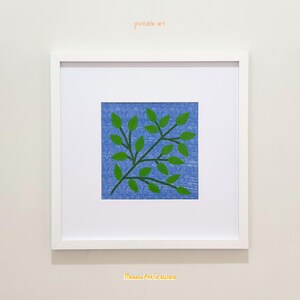 May include: A square white frame containing a print of a green leafy branch on a textured blue background. The text "printable art" appears above the frame, and the text "Meadow And Grassland" is printed in yellow below the frame.