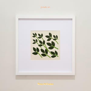 May include: A square white frame containing a print with a cream background and dark green leaf illustrations. The text "printable art" appears in orange above the frame, and "Meadow And Grassland" is printed in yellow below the frame.