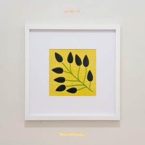 May include: A square framed print featuring a yellow background with a subtle pattern and a central green stem with dark black, oval-shaped leaves. The white frame includes a white mat board. The text "printable art" and "Meadow And Grassland" appear.