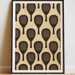 May include: A framed vertical wall art print featuring a repeating pattern of dark brown paddle tennis rackets arranged in a grid on a light beige background. The rackets are depicted with a perforated surface and a solid handle in a flat graphic style.