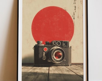 Può includere: Stampa incorniciata di una fotocamera nera vintage con obiettivo rosso, su sfondo di un grande cerchio rosso e sfondo crema. La fotocamera poggia su una superficie di legno, creando un'estetica retrò.
