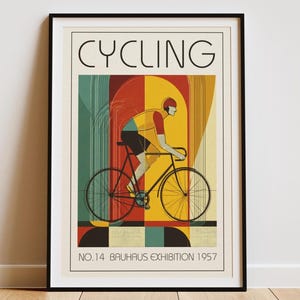 May include: Framed art print with a cycling theme. The poster shows a cyclist in yellow and red clothing on a black bicycle. The word "CYCLING" is at the top, with "NO.14 BAUHAUS EXHIBITION 1957" at the bottom. The background has vertical stripes.