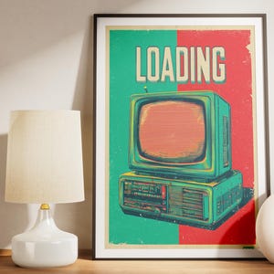 Könnte beinhalten: Gerahmtes Poster mit einer Retro-Fernseher-Illustration und dem Wort "LOADING". Der Hintergrund ist grün und rot. Eine weiße Lampe und Vase stehen auf einer Holzoberfläche, mit einer kleinen braunen Vase.