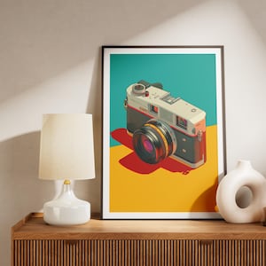 May include: A framed art print featuring a vintage camera illustration. The camera is depicted in a pop art style with a black and silver body, a large lens, and a red shutter button. The background is divided into teal, red, and yellow sections.
