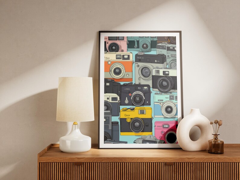 Pu&ograve; includere: Una stampa artistica incorniciata con un collage di fotocamere vintage in vari colori, tra cui rosa, arancione, nero e giallo. Le fotocamere sono disposte su uno sfondo azzurro chiaro, creando un'estetica retr&ograve;. La stampa &egrave; esposta su una superficie di legno.