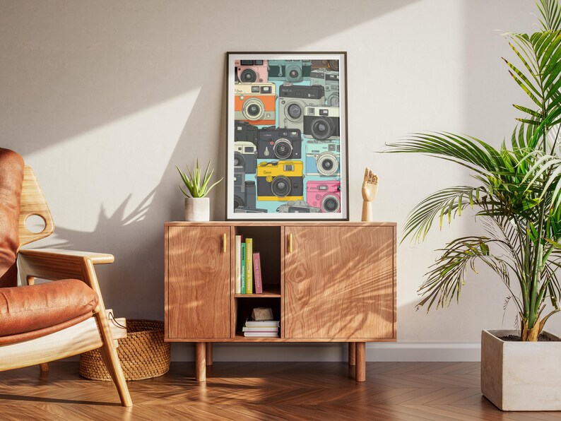 Pu&ograve; includere: Una stampa artistica incorniciata con un collage di fotocamere vintage in vari colori, tra cui rosa, giallo e turchese. La stampa &egrave; esposta su un mobile in legno con una piccola pianta e una scultura di mano in legno.