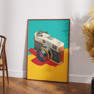 May include: A framed art print featuring a vintage camera illustration. The camera is white, black, and orange, with a large lens. The background is divided into teal, yellow, and red sections. The print is displayed on a wooden floor.