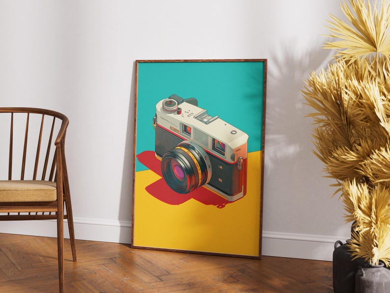 May include: A framed art print featuring a vintage camera illustration. The camera is white, black, and orange, with a large lens. The background is divided into teal, yellow, and red sections. The print is displayed on a wooden floor.