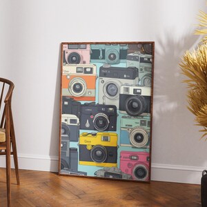 Pu&ograve; includere: Una stampa artistica incorniciata con un collage di fotocamere vintage in vari colori, tra cui rosa, giallo e nero. Le fotocamere sono disposte in un motivo ripetuto su uno sfondo azzurro, creando un'estetica retr&ograve;.