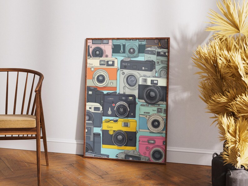 Pu&ograve; includere: Una stampa artistica incorniciata con un collage di fotocamere vintage in vari colori, tra cui rosa, giallo e nero. Le fotocamere sono disposte in un motivo ripetuto su uno sfondo azzurro, creando un'estetica retr&ograve;.