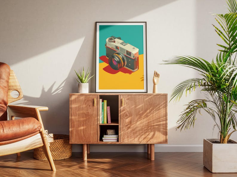 May include: A framed art print featuring a vintage camera illustration. The camera is depicted in a retro style with a teal, yellow, and red color scheme. The print is displayed on a wooden cabinet in a living room setting.