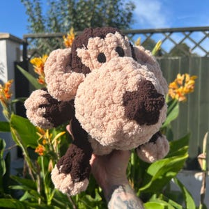 May include: A plush stuffed animal toy crafted from chunky yarn in dark brown and light beige. The creature features a large, rounded snout, prominent ears, and dark circular eyes, with a textured, soft appearance throughout its entire body.
