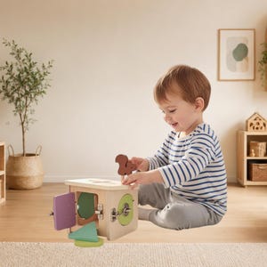 May include: A wooden activity cube featuring a light wood finish, a brown squirrel-shaped topper, and a hinged purple door. The cube includes a circular green panel with a metal latch and a triangular green block resting on the floor surface.