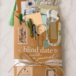 May include: A brown paper envelope labeled blind date with a journal, tied with white ribbon and twine. It contains stationery items including pens, a bookmark with a green tassel, a floral paperclip, a wax seal, and decorative paper ephemera.