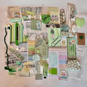 Peut inclure: Une collection de papeterie et d'accessoires sur le th&egrave;me du vert, comprenant des stylos, des autocollants, un chouchou, un agenda et un porte-monnaie. Les articles sont dispos&eacute;s sur une surface blanche.