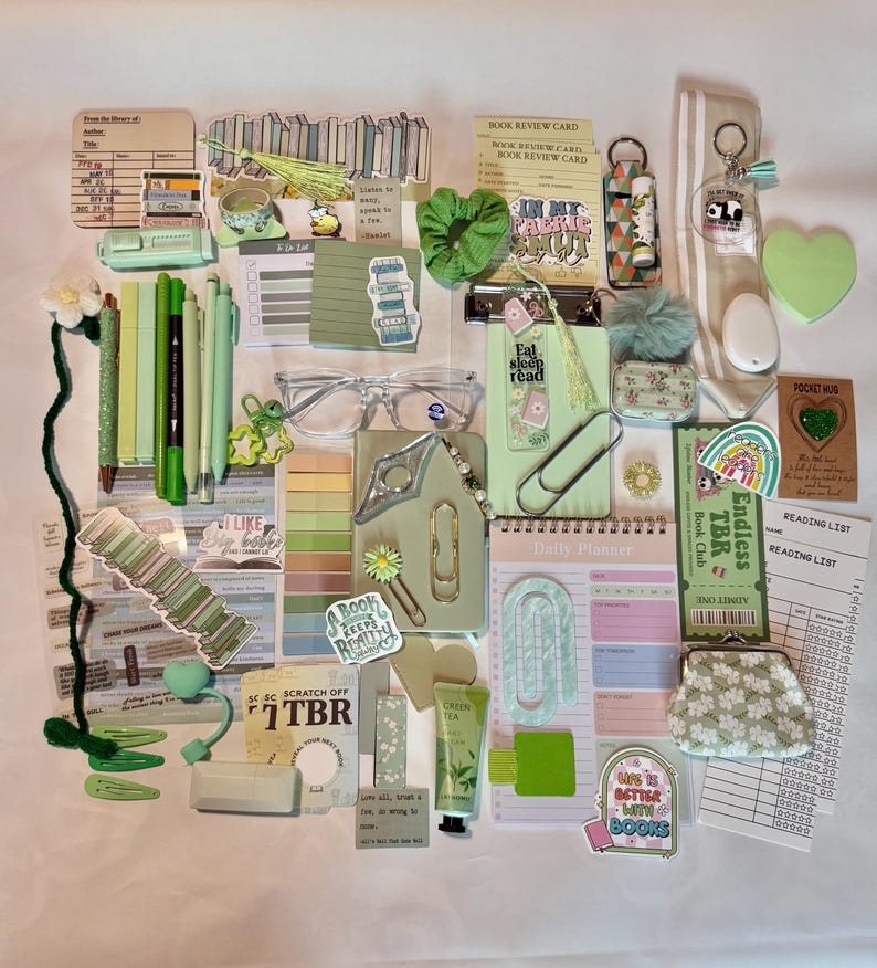 Peut inclure: Une collection de papeterie et d'accessoires sur le th&egrave;me du vert, comprenant des stylos, des autocollants, un chouchou, un agenda et un porte-monnaie. Les articles sont dispos&eacute;s sur une surface blanche.