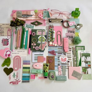 May include: A collection of stationery and reading accessories including a pink pencil case, a green notebook, pens, highlighters, bookmarks, stickers, a pink hair clip, green hair claw, pink glasses, and various paper goods with reading-themed text.