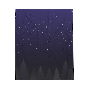 Puede incluir: Una manta rectangular con un degradado de cielo nocturno en color morado oscuro que se vuelve negro en la parte inferior. El diseño incluye un patrón de estrellas doradas y blancas dispersas de varios tamaños y una silueta de pinos.