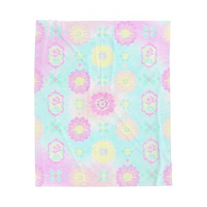 May include: A pastel-colored blanket with a repeating floral pattern. The design features pink, yellow, and blue flowers, along with decorative elements. The blanket has a soft, tie-dye appearance.