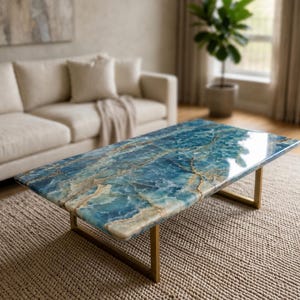Könnte beinhalten: Rechteckiger Couchtisch mit blau-goldener Marmorplatte. Der Tisch hat ein goldenes Metallgestell und steht auf einem beigefarbenen Webteppich. Der Raum zeigt ein beiges Sofa und eine Topfpflanze.