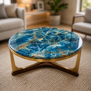 Puede incluir: Mesa de centro redonda con tapa azul efecto mármol y estructura metálica dorada. La base es de madera oscura. La superficie de la mesa presenta un llamativo patrón de vetas azules y doradas, añadiendo elegancia a cualquier salón. El diámetro es de unos 90 cm.
