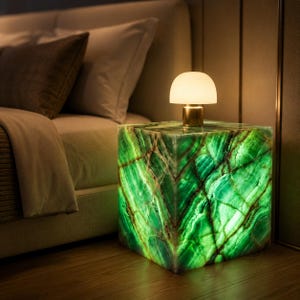 May include: A square side table crafted from translucent green stone with prominent white veining, illuminated from within to create a glowing effect. A small, dome-shaped lamp with a metallic base sits on the flat top surface of the cube.