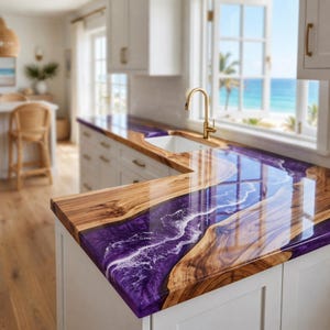 Op de afbeelding: Een L-vormig aanrechtblad met een houten blad met natuurlijke randen, geïntegreerd met een glanzend, dieppaars epoxyhars rivierontwerp dat stromend water met witte schuimaccenten nabootst, gecombineerd met een goudkleurige kraan.