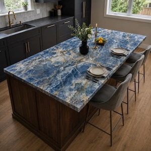 Op de afbeelding: Keuken eiland met een opvallend blauw marmeren aanrechtblad met gouden adering. Het eiland heeft een donkere houten basis en is omgeven door grijze barkrukken. Een vaas met bloemen, kaarsen en couverts sieren het aanrecht.