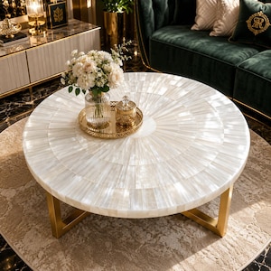 May include: A round coffee table featuring a white iridescent mother-of-pearl tiled surface arranged in a radial pattern, supported by a gold-toned metal base. A gold tray holds a clear glass vase with white flowers and a small gold lidded jar.