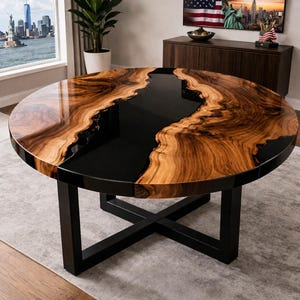 Puede incluir: Una mesa redonda de madera con un centro de resina epoxi negra. La mesa presenta un patrón de vetas de madera natural en tonos marrones y negros. Se apoya en una base de metal negro. La mesa tiene aproximadamente 122 cm de diámetro.