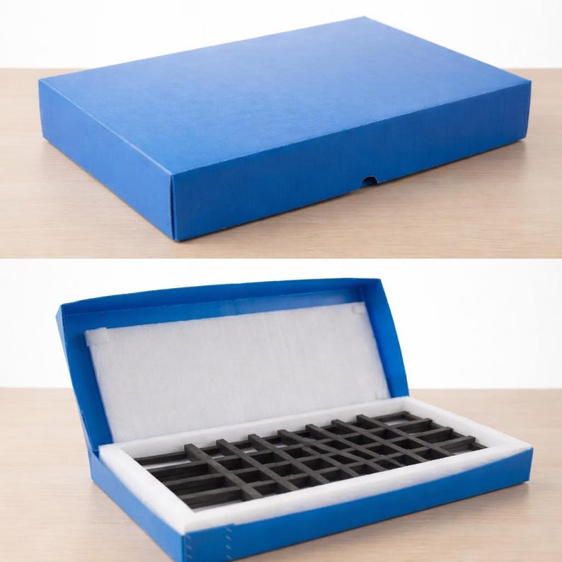 May include: A rectangular blue storage box with a lid. The interior features a white foam lining and a black grid-patterned insert designed for organizing small items. The box is shown both closed and open to reveal the internal compartments.