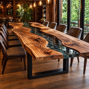 May include: A large dining table featuring two thick, natural-edge wood slabs with a central river-like inlay of clear resin filled with smooth, dark grey river stones. The table is supported by a sturdy, black metal U-shaped frame base.