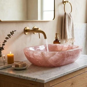 Luxury bathroom interior featuring a pink rose quartz vessel sink on marble countertop with modern brass faucet