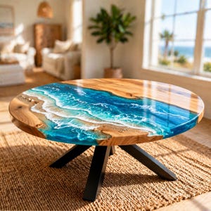 Pode incluir: Uma mesa de centro redonda com um tampo de madeira e um design de resina azul que se assemelha a ondas do oceano. A mesa tem uma base de metal preto e assenta sobre um tapete tecido. O diâmetro da mesa é de aproximadamente 100 cm.