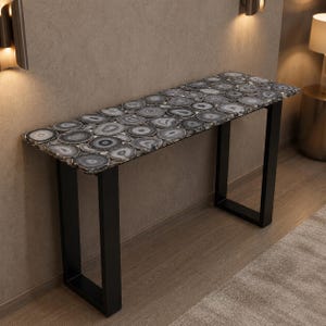 May include: A rectangular console table with a top made of gray and white agate slices. The table has a black metal frame. The table is approximately 48 inches long, 14 inches wide, and 30 inches high.
