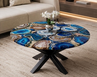 May include: A round coffee table featuring a tabletop composed of polished blue and brown agate slices embedded in a clear resin surface. The table is supported by a black metal base with four intersecting legs and holds a small white orchid.