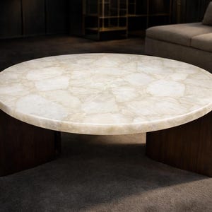 Pode incluir: Uma mesa de centro redonda com um tampo de pedra clara e estampada. A mesa tem uma base de madeira castanha escura com um design curvo. A mesa está numa sala de estar.