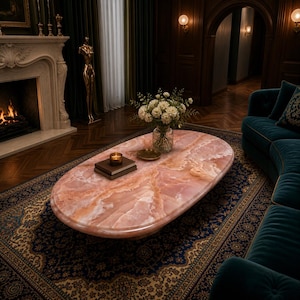 May include: An oval pink onyx coffee table with a polished surface. The table is in a luxurious living room, with a patterned blue rug, a teal sofa, and a fireplace. A candle and books are on the table.